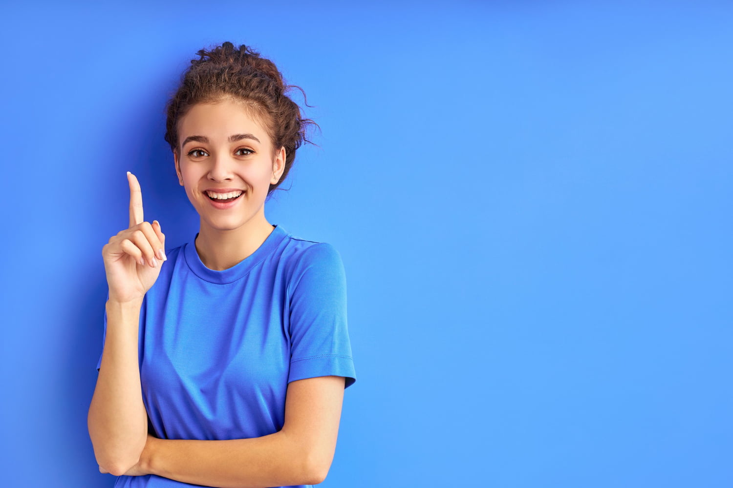 mulher de cabelo amarrado em um fundo azul levantando um dedo.
