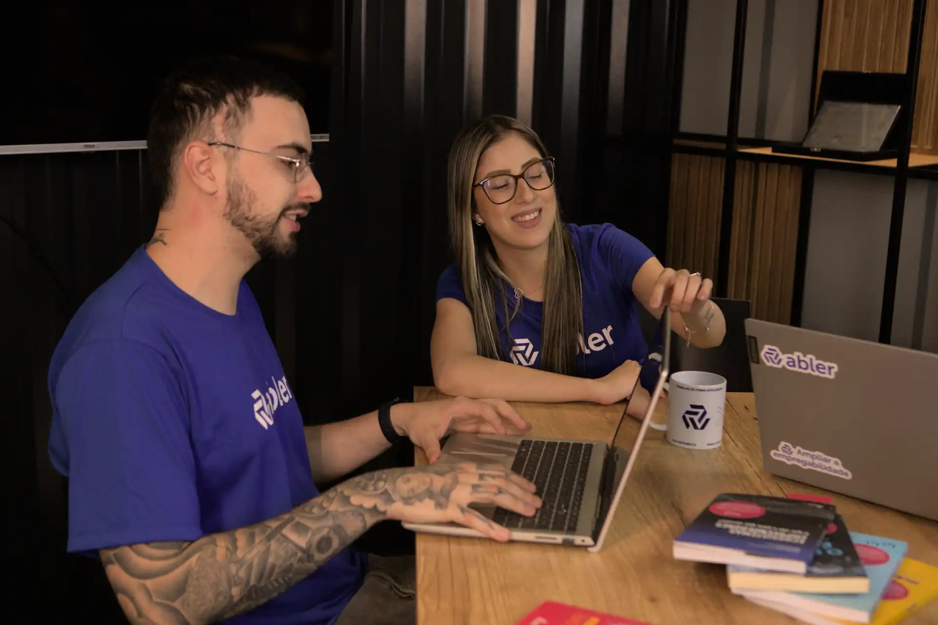 Profissionais engajados em trabalho de treinamento e desenvolvimento, colaborando em ambiente de escritório com laptops e materiais de apoio.