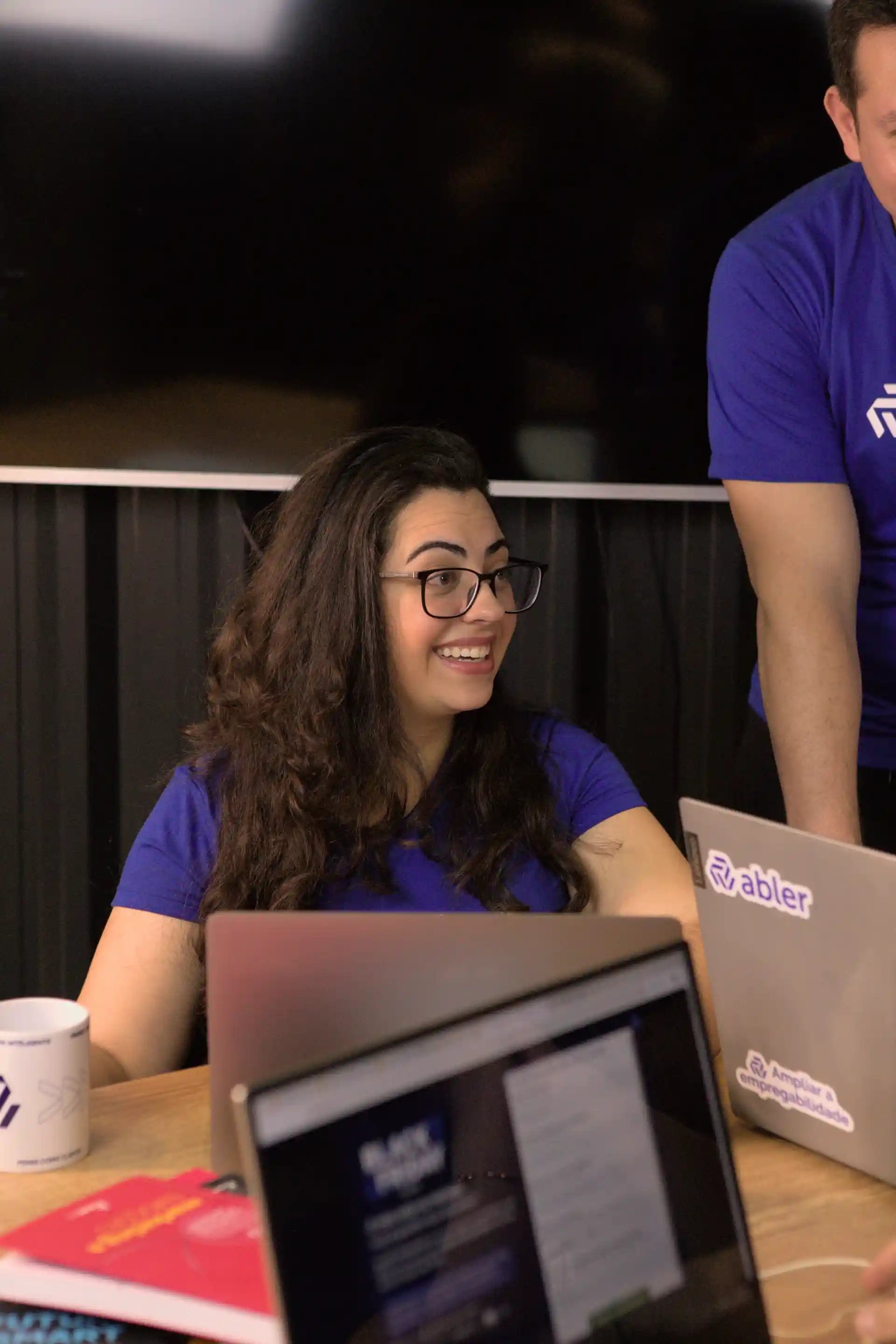 Funcionária sorridente em ambiente de trabalho colaborativo no Dia do Trabalhador, refletindo a alegria e a dedicação dos profissionais.