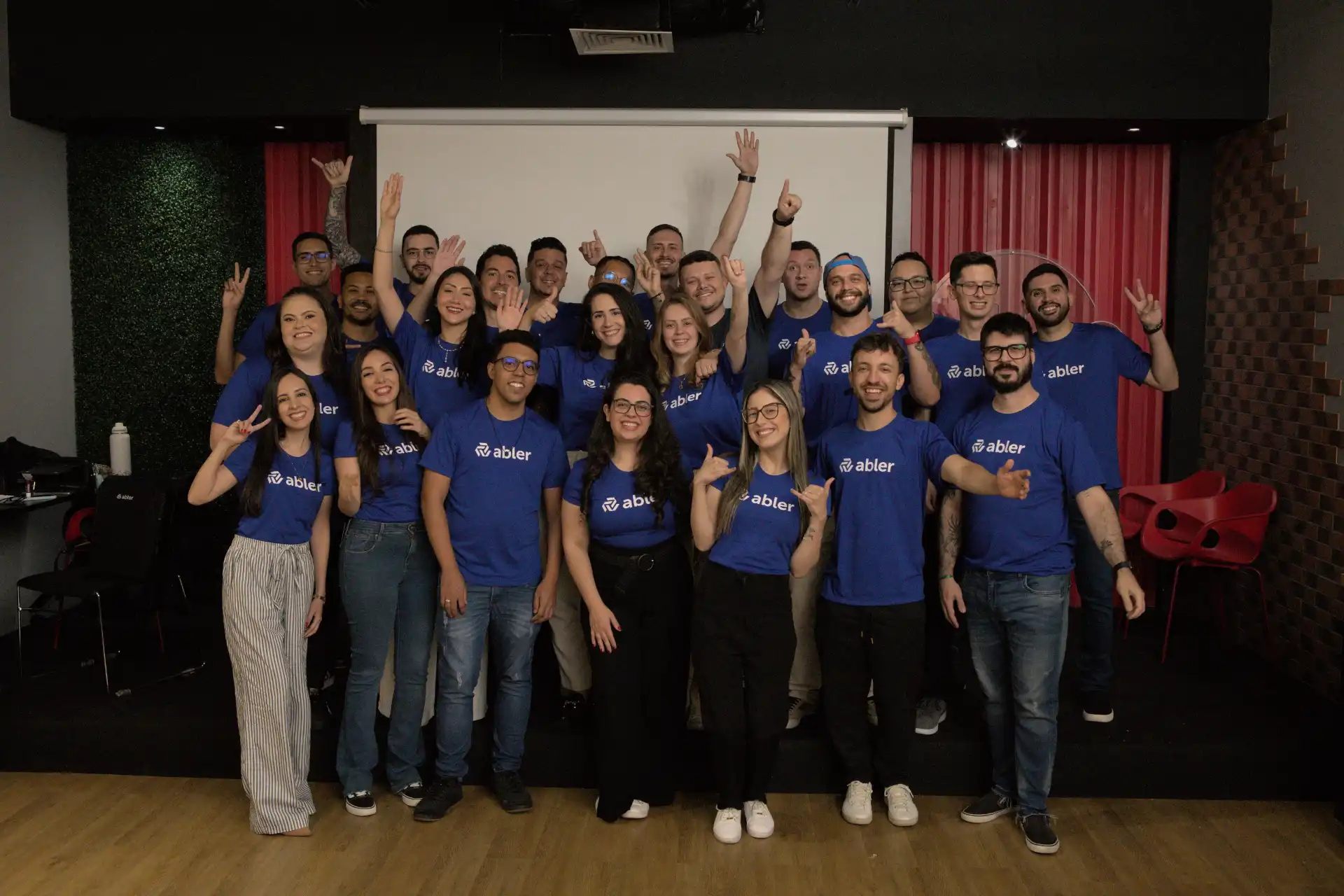 Equipe reunida em evento de inovação empresarial, todos vestidos com camisetas azuis. Entusiasmo e colaboração em destaque.