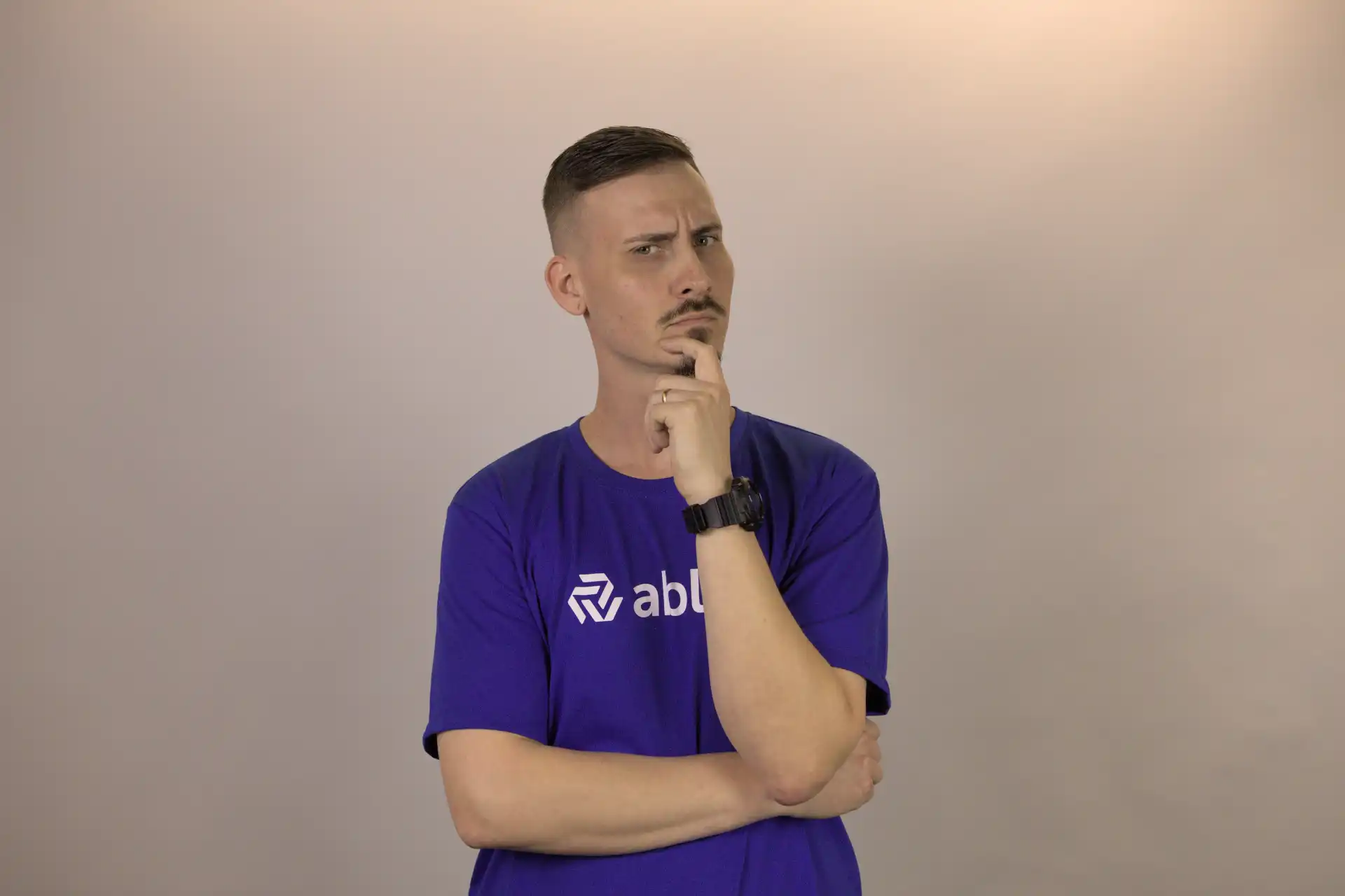 Homem pensativo em uma camiseta roxa, refletindo sobre o que não fazer em diversas situações. O fundo é neutro, destacando a expressão contemplativa.