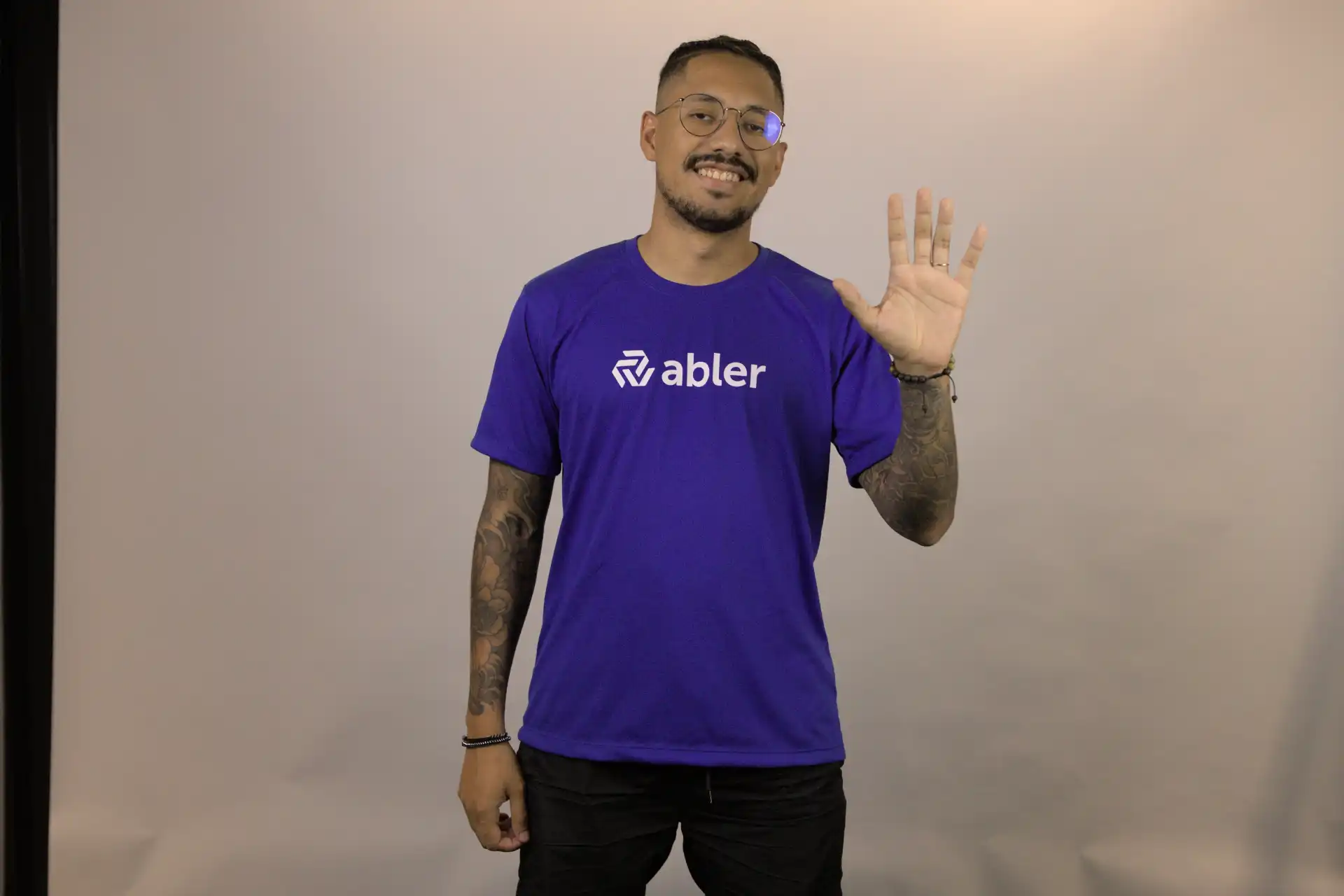 Homem sorridente vestindo camiseta roxa da marca Abler, levantando a mão em um gesto de saudação. Dicas sobre erros comuns.