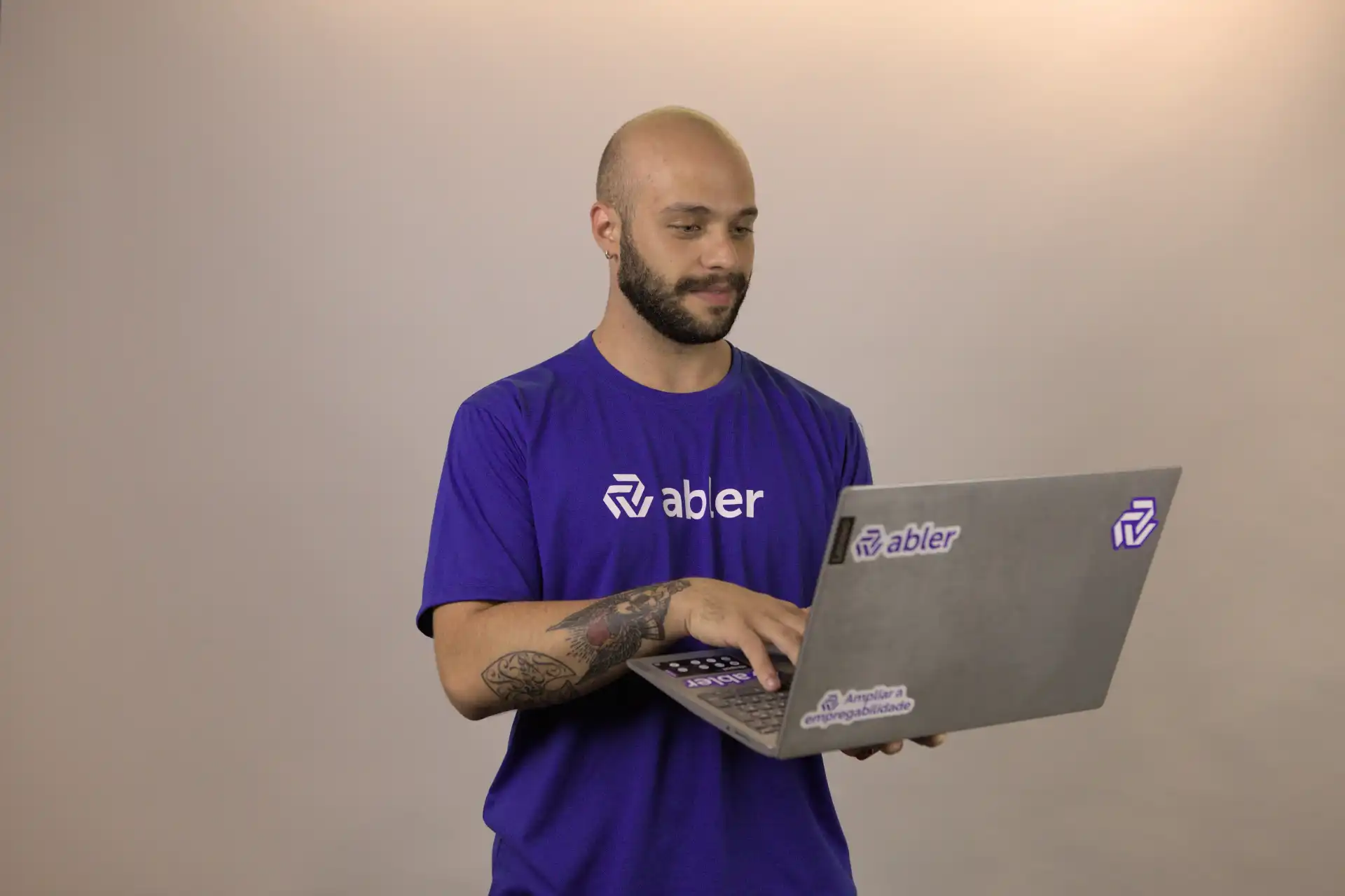Homem usando um laptop em uma plataforma de recrutamento, vestido com uma camiseta roxa da marca abler, sorrindo enquanto interage com a tela.