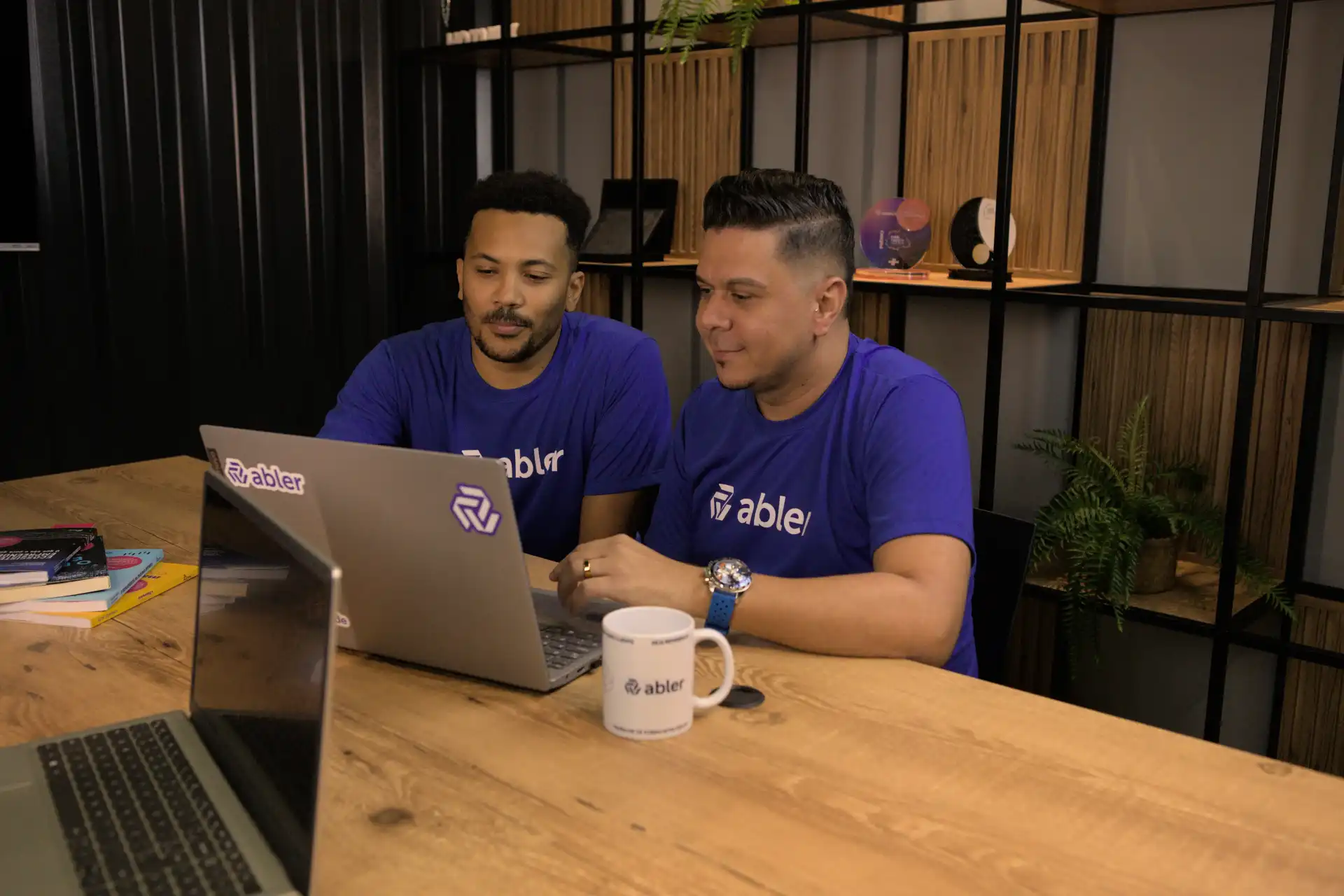 Dois profissionais em análise comportamental colaborando em um laptop em um ambiente de escritório moderno. Com foco na análise e estratégia.