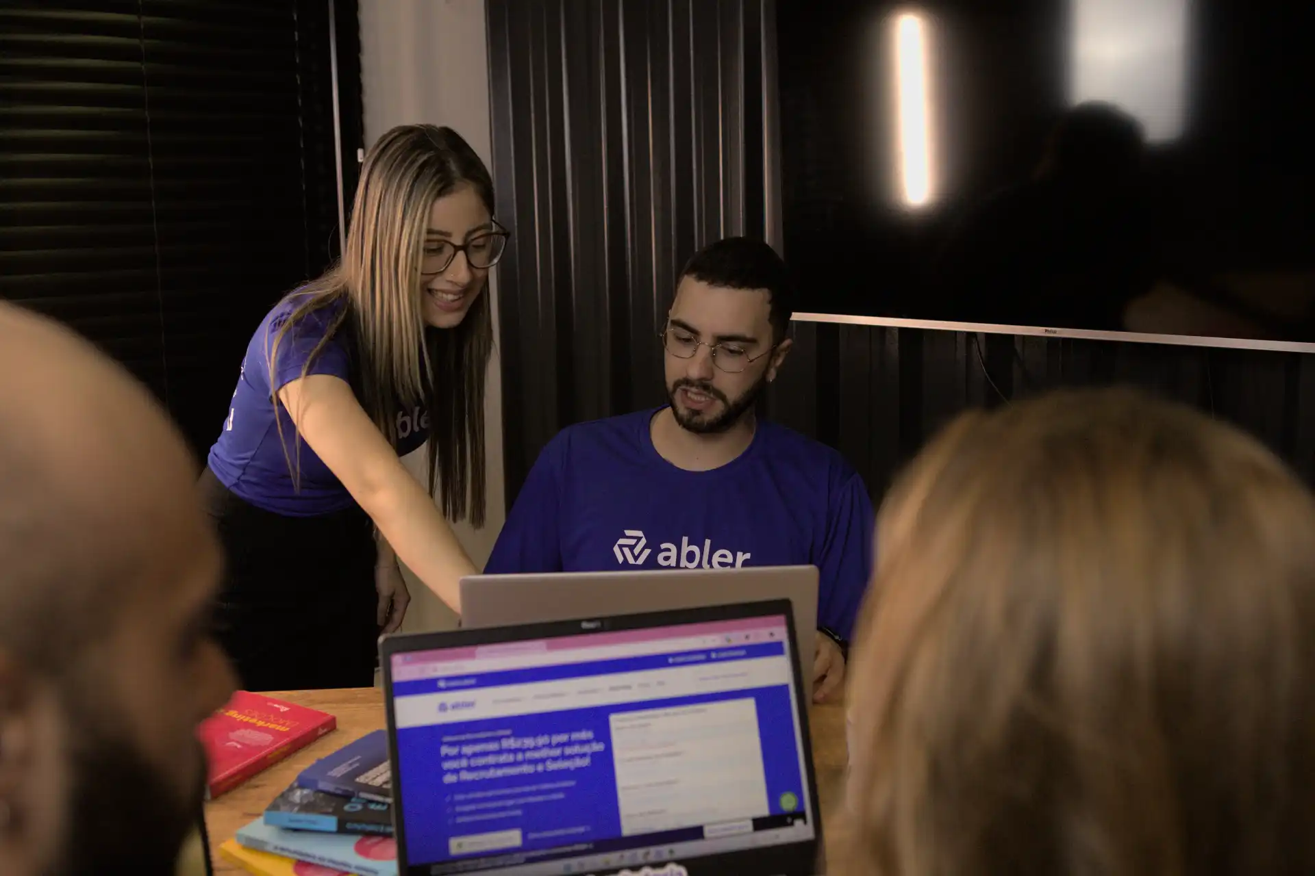 Grupo de profissionais colaborando em análise de dados em um ambiente de trabalho moderno. Um deles interage com um laptop enquanto outros observam.