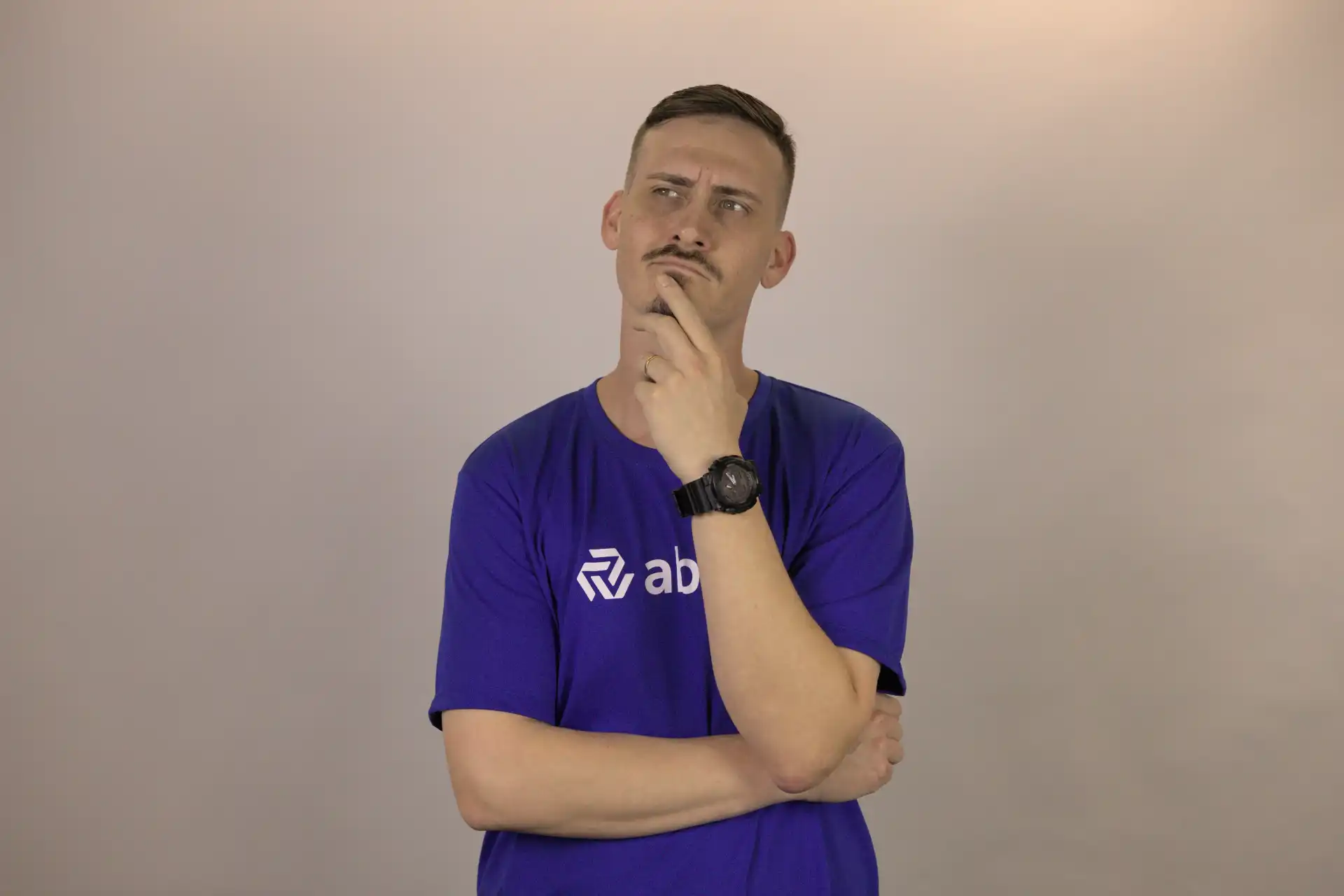 Um profissional de RH pensativo, vestindo uma camiseta azul, reflete sobre suas atividades. A imagem destaca a importância dos profissionais de RH na gestão de pessoas.