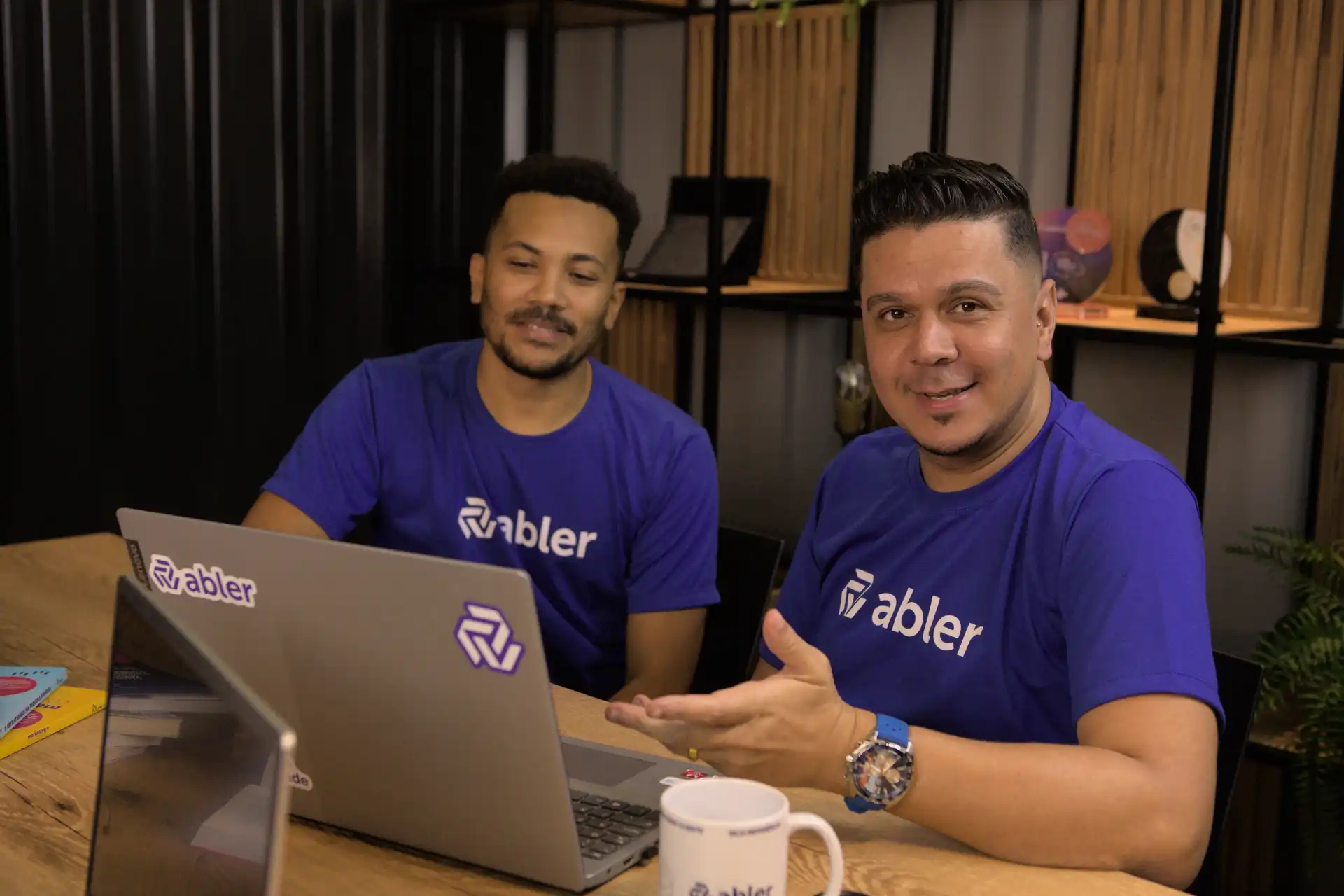 Imagem de profissionais discutindo estratégias de aquisição de talentos em um ambiente de trabalho moderno, com computadores e a logo da empresa abler visível.