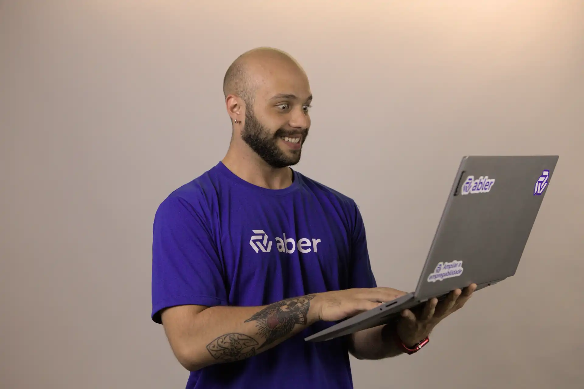 Homem sorridente usando um laptop, destacado pela automação e tecnologia. Ele veste uma camiseta azul com o logo da empresa.