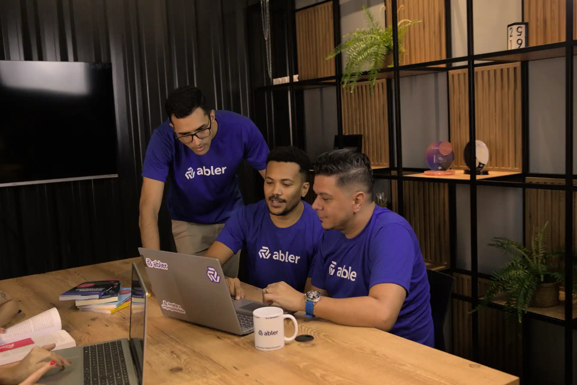 Imagem de três profissionais analisando um processo de recrutamento e seleção em um laptop, em ambiente colaborativo e produtivo.