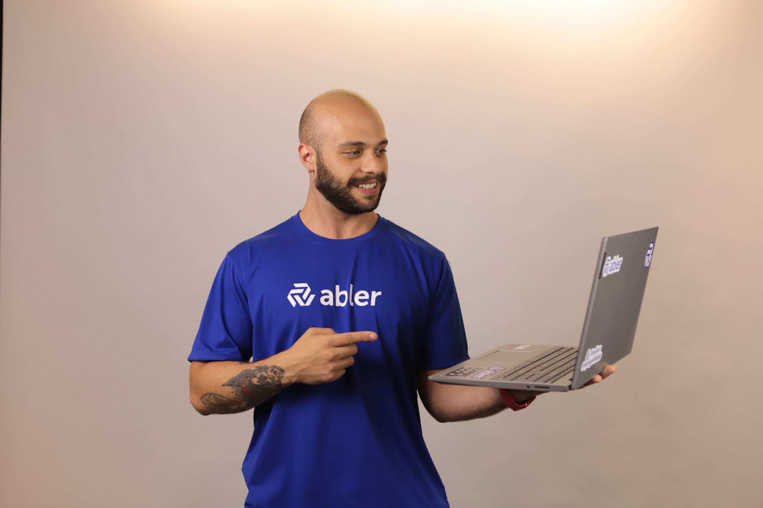 Profissional da abler segurando um notebook e apontando para a tela durante uma atividade de recrutamento e seleção. A imagem representa a dependência de processos manuais e decisões tomadas apenas após a abertura de vagas, ilustrando os desafios e o custo invisível de um recrutamento reativo para equipes de RH que buscam mais eficiência e previsibilidade na contratação de talentos.